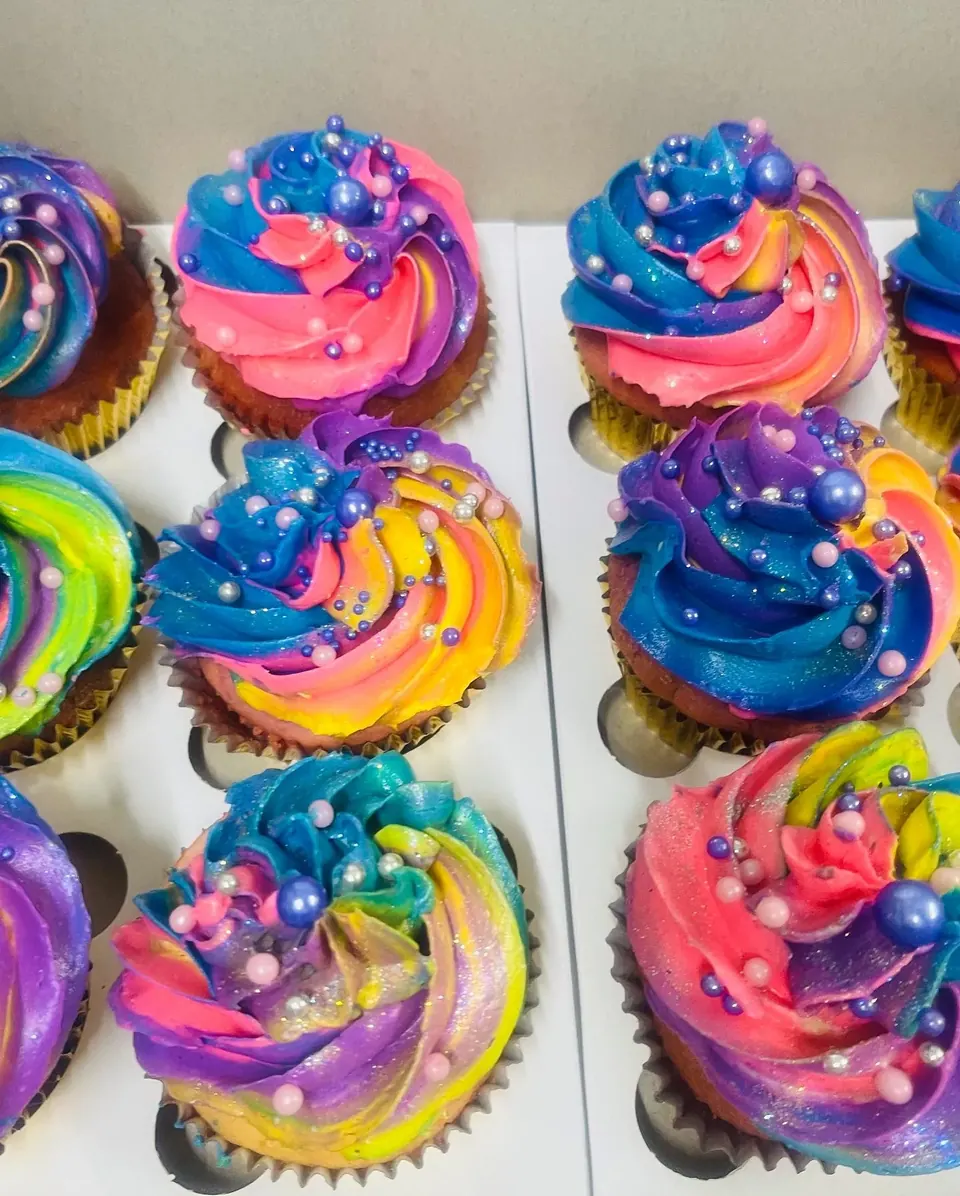 Cupcakes piped with rainbow swirls of buttercream and pearl sprinkles