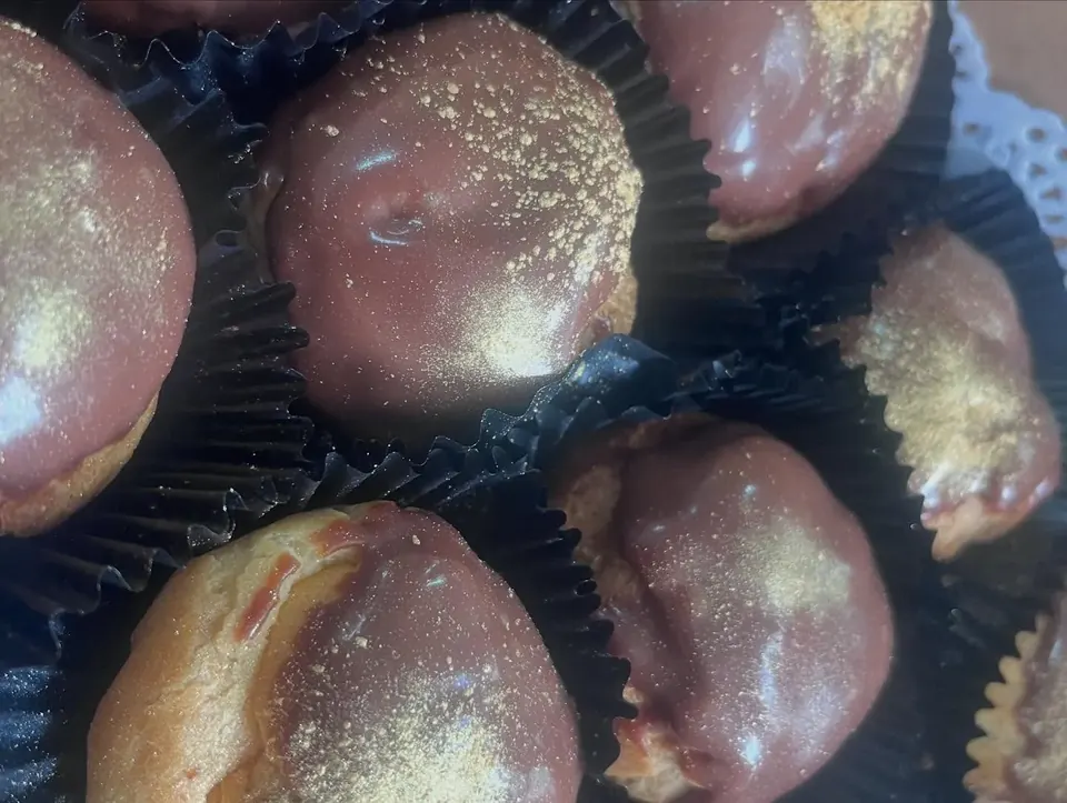 Chocolate glazed doughnuts dusted with edible gold shimmer in paper cases