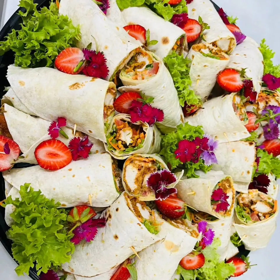 Platter of chicken wraps with frilly lettuce, halved strawberries and edible flowers