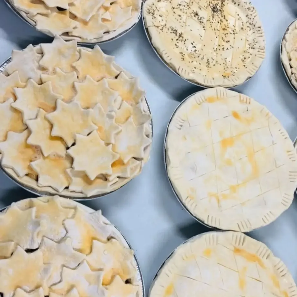 Family pies in foil dishes, ready to bake, some topped with pastry stars and some with scored crusts