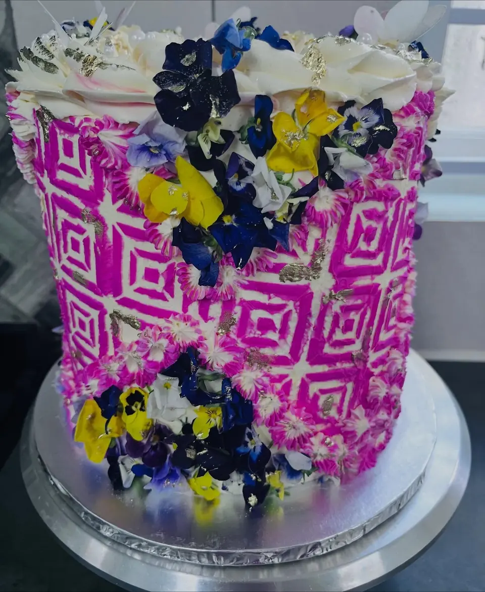 Tall celebration cake with a bright pink geometric pattern, cream rosettes and edible pansies