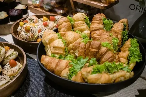 Buffet table with a large bowl of filled croissants and a bowl of seeded bagels with cherry tomatoes