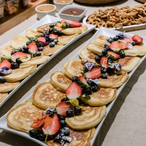 Long platters of fluffy pancakes topped with strawberries, blueberries and edible flowers